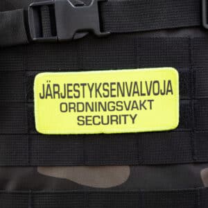 Järjestyksenvalvoja Tarranauhamerkki Keltainen 3 kielinen, musta teksti keltaisella pohjalla, tarranauhakäyttöinen viranomaismerkki, 12 x 5 cm, 3-kielinen versio jossa sanat järjestyksenvalvoja, ordningsvakt ja security.