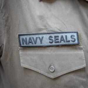 Navy Seals Kangasmerkki Vihreämusta, suorakulmion muotoinen kangasmerkki, jossa lukee mustalla tekstillä "NAVY SEALS", vahvennetut reunat, ommellaan, silitetään tai liimataan kiinni haluttuun tuotteeseen.